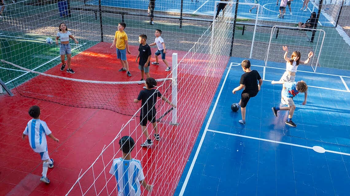 Imagen de cancha con pelotas y niños jugando